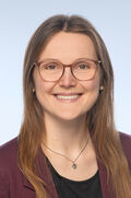 Portraitfoto einer Frau mit langen braunen Haaren und Brille, die freundlich in die Kamera lächelt.
