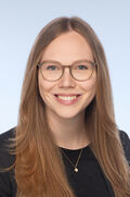 Portraitfoto einer Frau mit langen braunen Haaren und Brille, die freundlich in die Kamera lächelt.