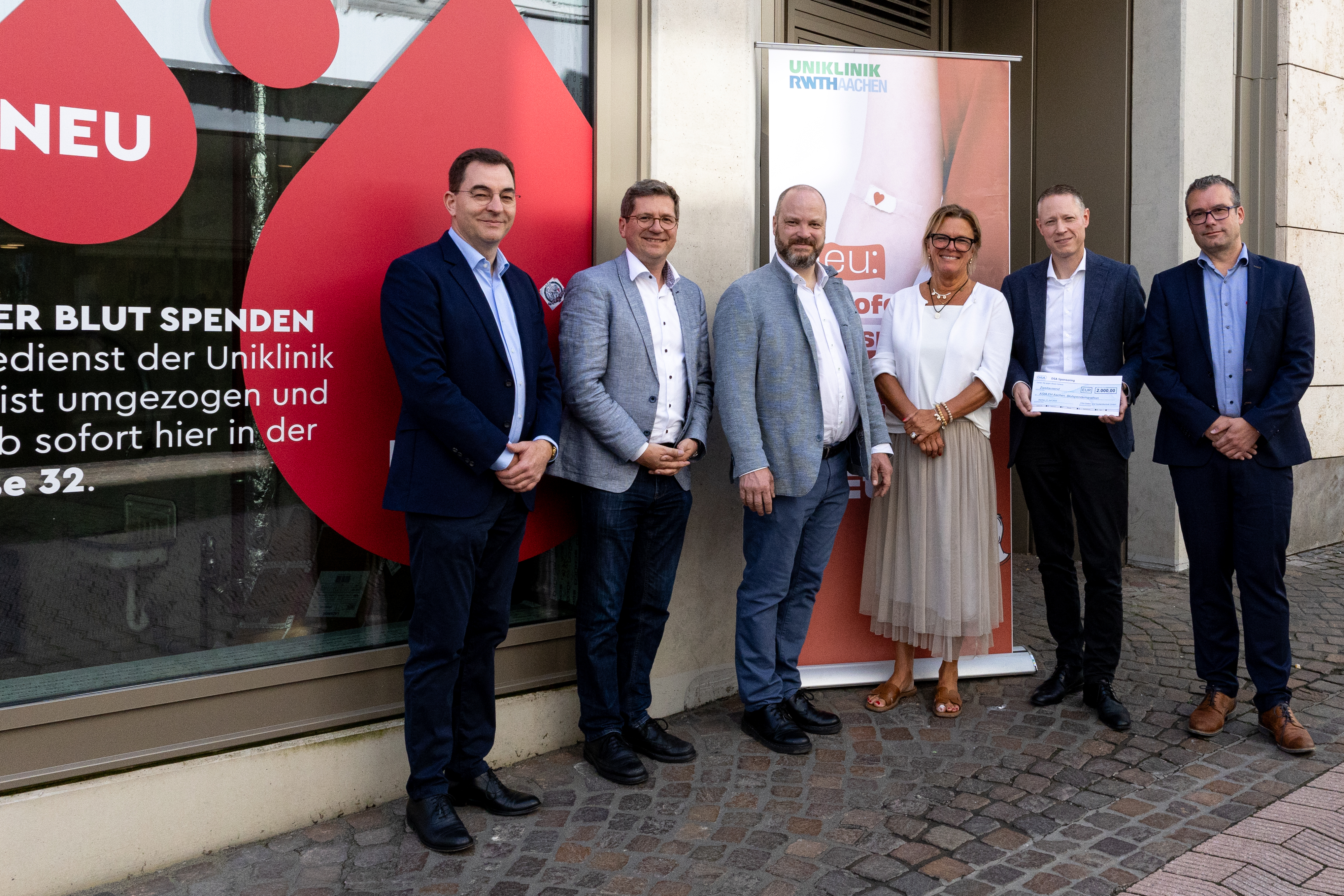 Fünf Herren und eine Dame stehen vor einem Roll-up.