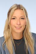 Junge Frau mit blonden langen Haaren und braunen Augen in einem blauen Blazer.