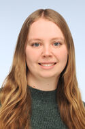 Porträtfot einer Frau mit langen brauen Haaren und einem dunkelgrauen Pullover. Sie lächelt freundlich in die Kamera.