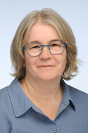 Porträtfoto einer Frau mit dunkelblonden, schulterlangen Haaren. Sie trägt eine Brille mit einem runden und einem eckigen Brillenglasrahmen.