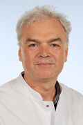 Portraitfoto eines Mannes mit kurzen, hellen Haaren im weißen Arztkittel.