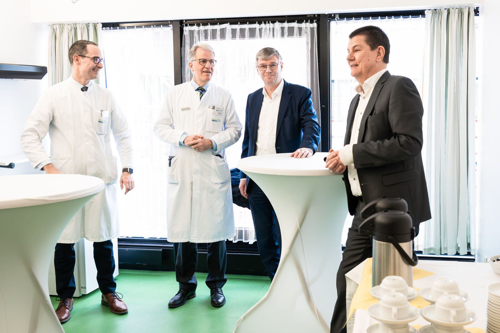 Zwei Herren in Anzügen, zwei in Kitteln