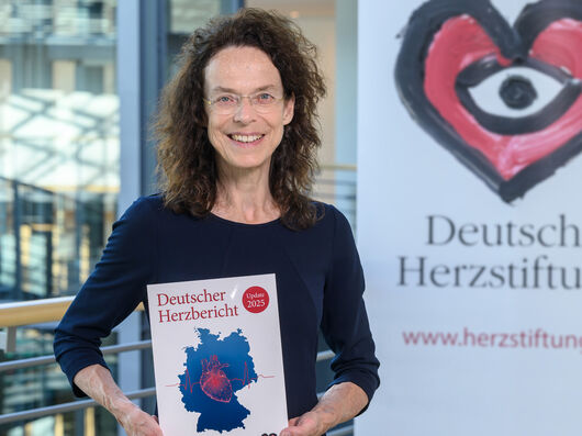 Ältere Frau mit braunen locken und Brille hält den Deutschen Herzbericht 2025 in den Händen