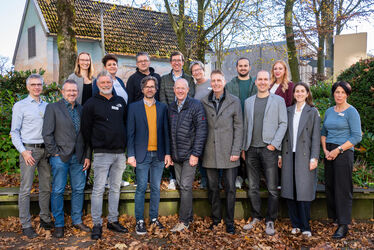 Teamfoto mit mehreren Frauen und Männern draußen vor einem Haus im Herbst.