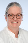 Porträtfoto einer Frau mit grauem Haar und Brille, die einen weißen Kittel trägt und freundlich in die Kamera lächelt.