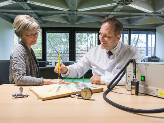 Ein Mann mit dunklen Haaren in einem weißen Arztkittel berät eine Frau mit blonden Haaren und einer gräulichen Jacke.