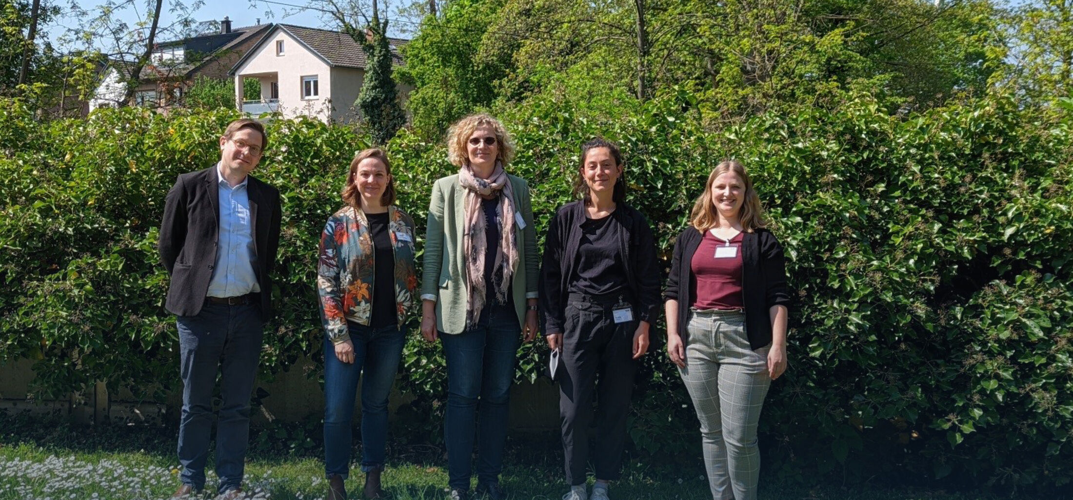 Team Bonn Fünf Personen stehen vor einer grünen Hecke, im Hintergrund sind Häuser sichtbar.
