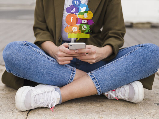 Junge Person sitzt im Schneidersitz mit dem Handy in der Hand