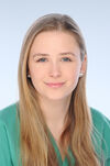Porträtfoto einer Frau mit blonden, langen Haaren. Sie trägt grüne medizinische Kleidung und lächelt freundlich in die Kamera.